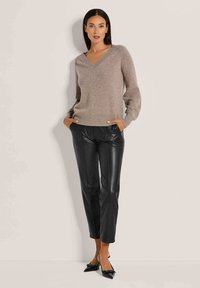 Beiger V-Ausschnitt-Pullover mit weichem Material, kombiniert mit schwarzen Leder-Hosen in schmaler Form mit Taschen, abgerundet mit spitzen Absätzen.