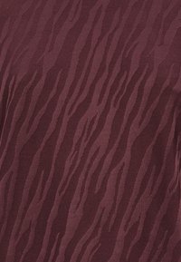 Bordeauxfarbener Stoff mit einem subtilen, tonalen Wellenmuster. Der Stoff hat eine glatte Textur mit einem leichten Glanz, der die Tiefe des Designs unterstreicht.