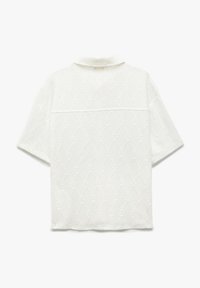 Camisa blanca de manga corta con un patrón de diamantes texturizado, con un cuello estrecho y una costura horizontal en la parte posterior.