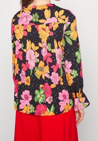 Blusa in tessuto nero con motivo floreale, caratterizzata da fiori vivi nei toni del rosa, arancione e verde, maniche lunghe e dettagli a pieghe.