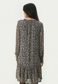 Lange mouwen jurk in zwart-wit paisley patroon, met een geplooide halslijn en een gelaagde rucheszoom, gemaakt van lichte, doorzichtige stof.