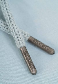 Cordones trenzados de color azul claro con aglets metálicos, grabados con "Reell". La textura es suave, contrastando con la tela tejida de los cordones.