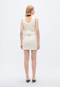 Άσπρο φόρεμα με υφή λουλουδιών, εφαρμοστή σιλουέτα, αμάνικο σχέδιο και φερμουάρ στο πίσω μέρος. Συνδυασμένο με μαύρες ψηλοτάκουνες πέδιλες ανοιχτής μύτης.