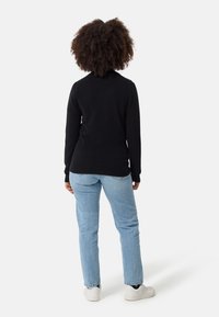 Musta paita pitkillä hihoilla ja pyöreällä kaula-aukolla, yhdistettynä vaaleansinisiin farkkuihin ja valkoisiin tennareihin. Tekstuurin näyttää olevan pehmeä ja mukava.