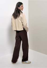 Veste beige texturée coupée, pantalon brun ample et baskets multicolores, présentant une coupe décontractée et une palette de couleurs neutres.