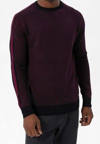 Pull ras du cou bordeaux à manches longues, avec poignets noirs côtelés et bandes latérales contrastantes rose foncé. Tissu en maille texturée avec une coupe ajustée.