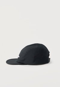 Μαύρο καπέλο πέντε πάνελ με επίπεδο γείσο, οπές αερισμού και μια μικρή υφασμάτινη ετικέτα στο πίσω μέρος σε λευκό απλό φόντο.