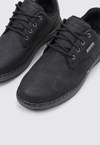 Schwarze Lederschuhe mit glatter Textur, runder Zehenpartie, Schnürdesign und kontrastierenden Nähten entlang der Sohle. Wasserdichtes Etikett sichtbar.