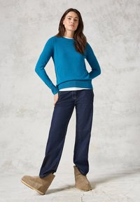 Pull turquoise à encolure ronde, associé à un jean bleu foncé et des bottines beige à la cheville. Couleur unie, détails de poignets et d'ourlet côtelés.