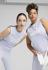 Svijetloplave bezrukavice s bijelim logom "PUMA", koje nose dvije osobe. Glatka tkanina, dizajn s okruglim izrezom, minimalistički stil.