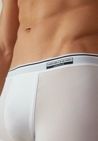 Weiße Boxershorts verfügen über eine weiche, netzartige Textur mit einem schwarz-weißen Bündchen. Das Logo ist auffällig auf dem Bündchen platziert.