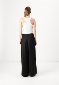 Pantalons larges noirs avec une finition satinée, associés à un débardeur blanc à rayures. La tenue présente une taille ajustée et deux poches arrière.