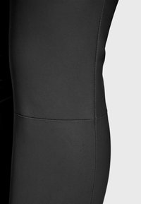 Crne hlače od umjetne kože s glatkom teksturom, s uskim krojem i vidljivim šavovima na području bedara.