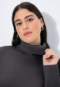 Maglione a collo alto di colore grigio scuro, realizzato in materiale a coste, con un collo alto e un motivo decorativo a rete sulle maniche.
