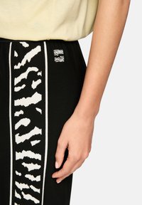 Black sweatpants featuring a white animal print stripe and a small logo patch at the waistband. Smooth texture, fitted design.