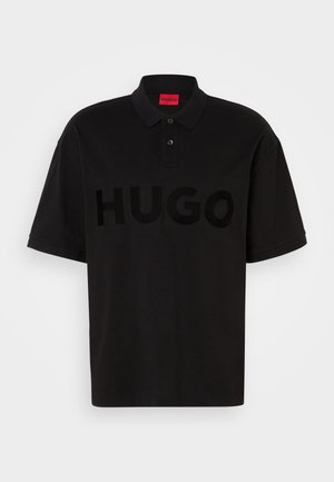 Black polo shirt made of cotton, featuring a large, tonal "HUGO" logo on the front, two-button collar, and short sleeves.