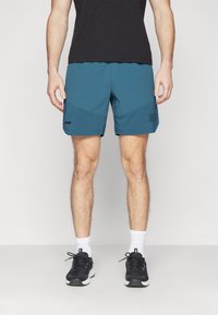 Teal träningsshorts med ett texturerat rutmönster i fållen, sidofickor och en svart logotyp. Bärs med svarta sneakers och vita strumpor.