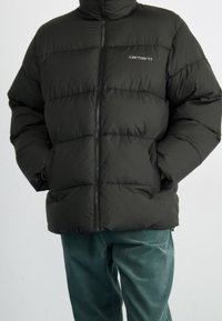 Sort oppustelig jakke med vandrette quiltede sektioner, høj krave og lynlåslukning. Bemærkelsesværdigt mærke logo på venstre bryst.