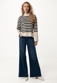 Pullover a righe in crema e nero con collo alto, abbinato a jeans a gamba larga blu scuro e scarpe color crema. Outfit semplice e casual.