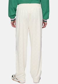 Witte loungebroek met een textuurpatroon, elastische tailleband en accenten aan de zijkant. Gecombineerd met een groen shirt met lange mouwen.