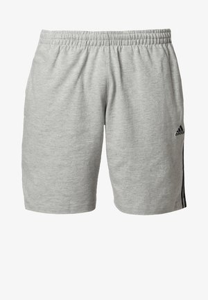 Mężczyzna idący w granatowej koszulce Adidas, jasnoszarych szortach z czarnymi paskami, czarnych skarpetkach i czarnych butach sportowych Adidas.