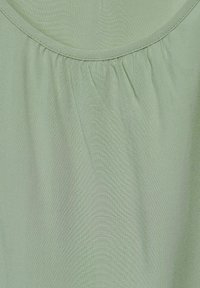 Blouse vert clair avec un col rond, présentant un tissu froncé le long du col, une texture lisse et un design doux et fluide.