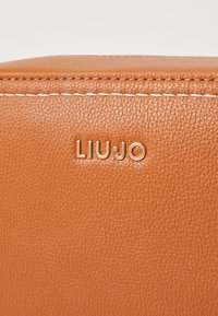Tote aus honigfarbenem Leder mit strukturierter Oberfläche. Ausgestattet mit weißem Nähen und dem goldfarbenen "LIU·JO"-Logo, das auffällig platziert ist.