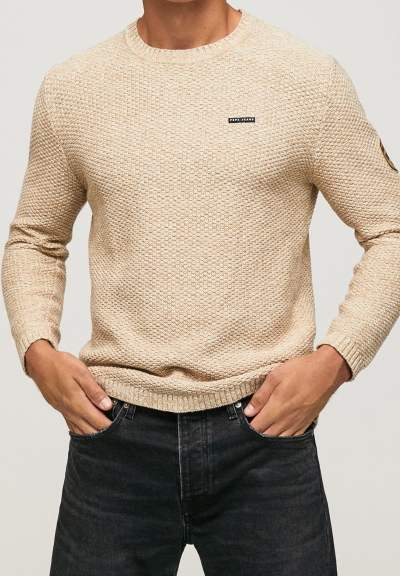 Beige gestrickter Pullover mit einem strukturierten Muster, Rundhalsausschnitt und gerippten Bündchen. Verfügt über ein kleines Markenlabel auf der Brust.