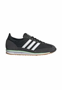 Zapatillas de ante negras con tres rayas blancas, puntera redondeada, cuello de cuero negro y suela de goma color caramelo con acento verde.