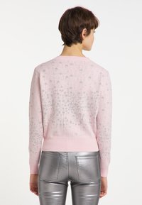 Pulover roz deschis cu un model de stele argintii, guler rotund și manșete cu dantelă, asortat cu pantaloni metalici argintii. Vedere din spate.