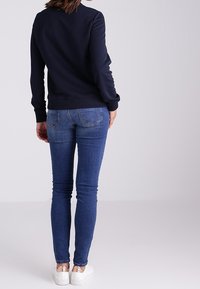 Felpa blu navy con maniche lunghe, abbinata a jeans skinny blu scuro. Le calzature presentano suole bianche con dettagli metallici.