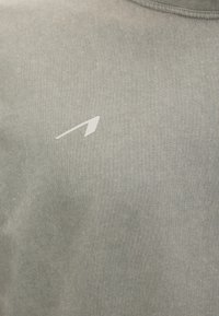 Κοντινή λήψη ανοιχτόχρωμου γκρι υφάσματος με ένα μικρό λευκό μινιμαλιστικό λογότυπο τυπωμένο στην περιοχή του στήθους.