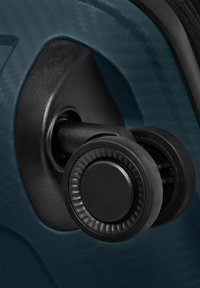 Gros plan sur des roues doubles pivotantes noires fixées à l'angle d'une valise rigide texturée bleu foncé.