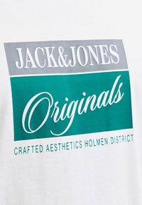 Tissu blanc avec un rectangle gris portant la mention « JACK&JONES » et un rectangle bleu canard avec « Originals » et un texte plus petit « Crafted Aesthetics Holmen District. »