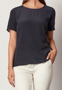 Blusa a maniche corte di colore blu navy in tessuto liscio con scollatura tonda; abbinata a pantaloni color crema, che mostrano una vestibilità rilassata.