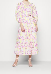 Abito lungo floreale giallo con motivo a marmorizzazione rosa e bianca, con scollatura a V, maniche a sbuffo, vita aderente e gonna a strati.