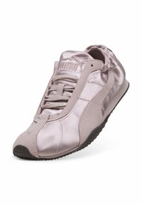 Ανοιχτό ροζ σατέν αθλητικό παπούτσι Puma με σουέντ ρίγες, υφασμένο μαύρο πέλμα και κορδόνι μπροστά, σε λευκό φόντο με κλίση.