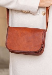Brown leather crossbody bag with a smooth texture, front flap, and contrasting stitching. Compact design featuring a shoulder strap.