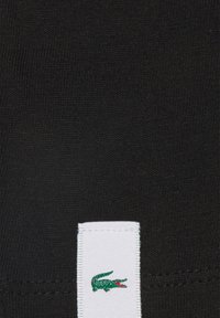 Tessuto di cotone nero con una texture a coste, caratterizzato da un'etichetta bianca con un logo di coccodrillo verde. Design semplice e minimalista.