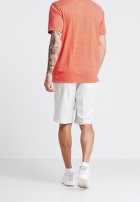 Röd- och vitrandig kortärmad skjorta i kombination med vita shorts. Tyget ser lätt ut och har en avslappnad passform med en subtil mönstertextur.