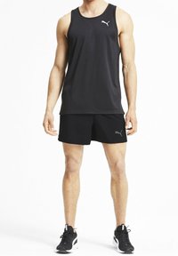 Svart sportstopp med rund hals, tillsammans med matchande svarta shorts. Har en grå Puma-logotyp på bröstet och sidan. Bärs med svarta sneakers.