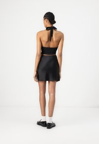 Black halter crop top with a tie closure at the back, paired with a black mini skirt. Features a smooth texture and a fitted silhouette.