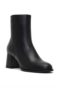 Bottine en cuir noir à bout arrondi et talon épais. Texture lisse, design minimaliste, sans matériel ou ornements visibles.