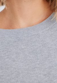 Hellgrauer Strickpullover mit geripptem Rundhalsausschnitt, der eine weiche Textur und glatte Oberfläche aufweist. Der Stoff wirkt leicht und lässig.