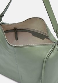 Zielona skórzana torebka o gładkiej fakturze, z zamknięciem na zamek błyskawiczny, wewnętrzną kieszenią i zorganizowanym kształtem. Wnętrze jest w jasnym kolorze.