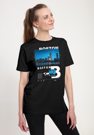 Sort t-shirt med et grafisk print af Bostons skyline i blå og hvid, med ordet "BOSTON" fremtrædende i forskellige størrelser.