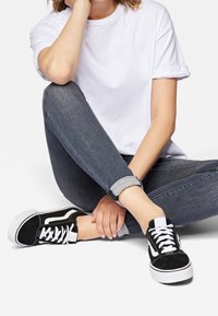 Svarta canvas-sneakers med vita detaljer, platt vit sula och snörning. Stylad med en enkel vit T-shirt och mörka denimjeans.