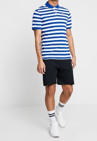 Blå och vit randig pikétröja med krage, kombinerad med svarta shorts. Vita sneakers och randiga crew-strumpor kompletterar looken.