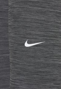 Grå atletisk tyg med ett strukturerat mönster. Har en vit Nike swoosh-logotyp på höger sida.