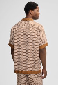 Man die met de rug naar ons staat, met een bijpassende bruin-witte gekleurde korte mouwen shirt en broek, met een effen bruine kraag en manchetten.